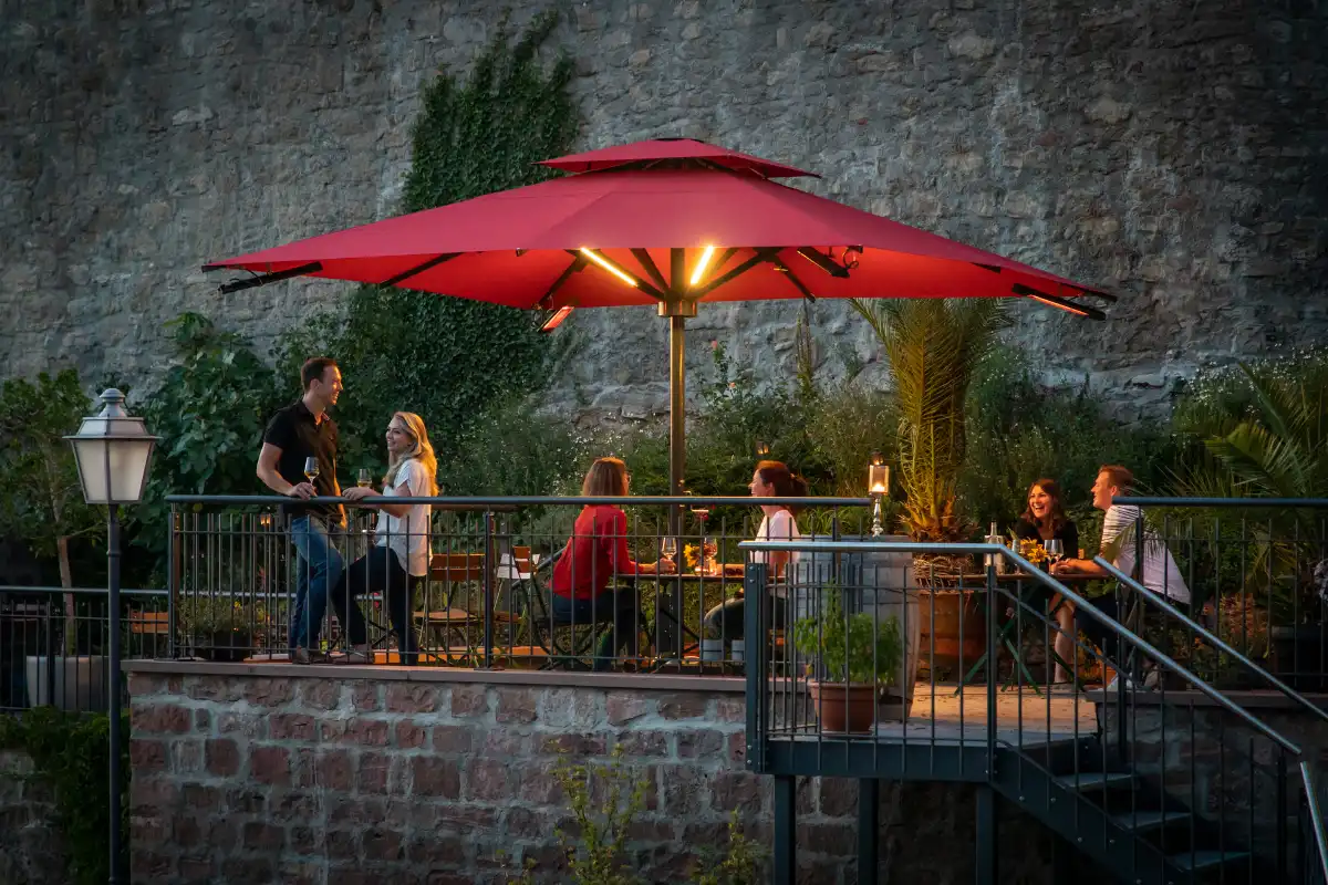 Abendliche Terrasse mit beleuchtetem rotem Sonnenschirm Gemütliche Abendstimmung in einem Außenbereich mit rotem Sonnenschirm und Menschen bei einem Drink