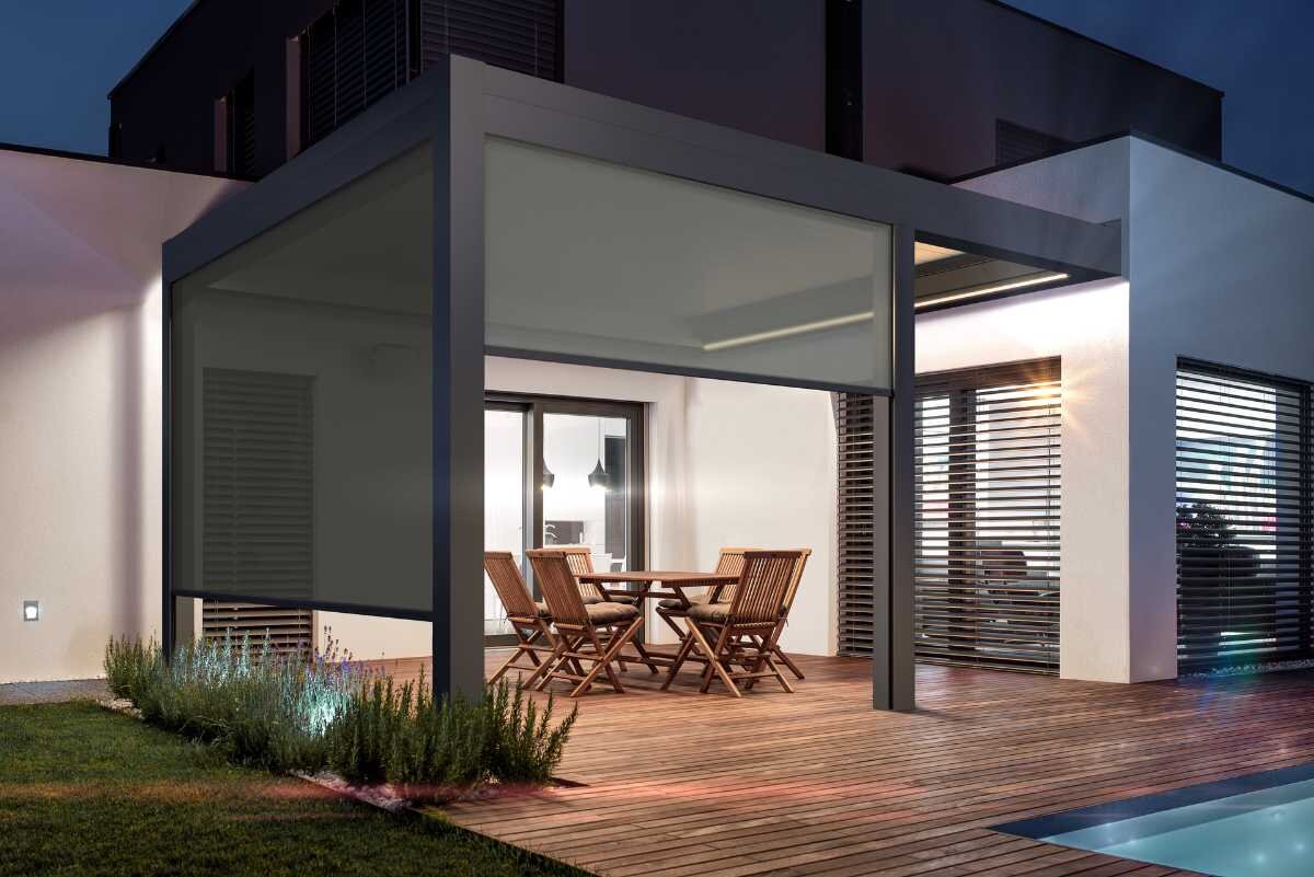 Terrassenüberdachung mit stilvollen Holzmöbeln bei Nacht Moderne Überdachung auf einer stilvollen Terrasse mit Holzstühlen